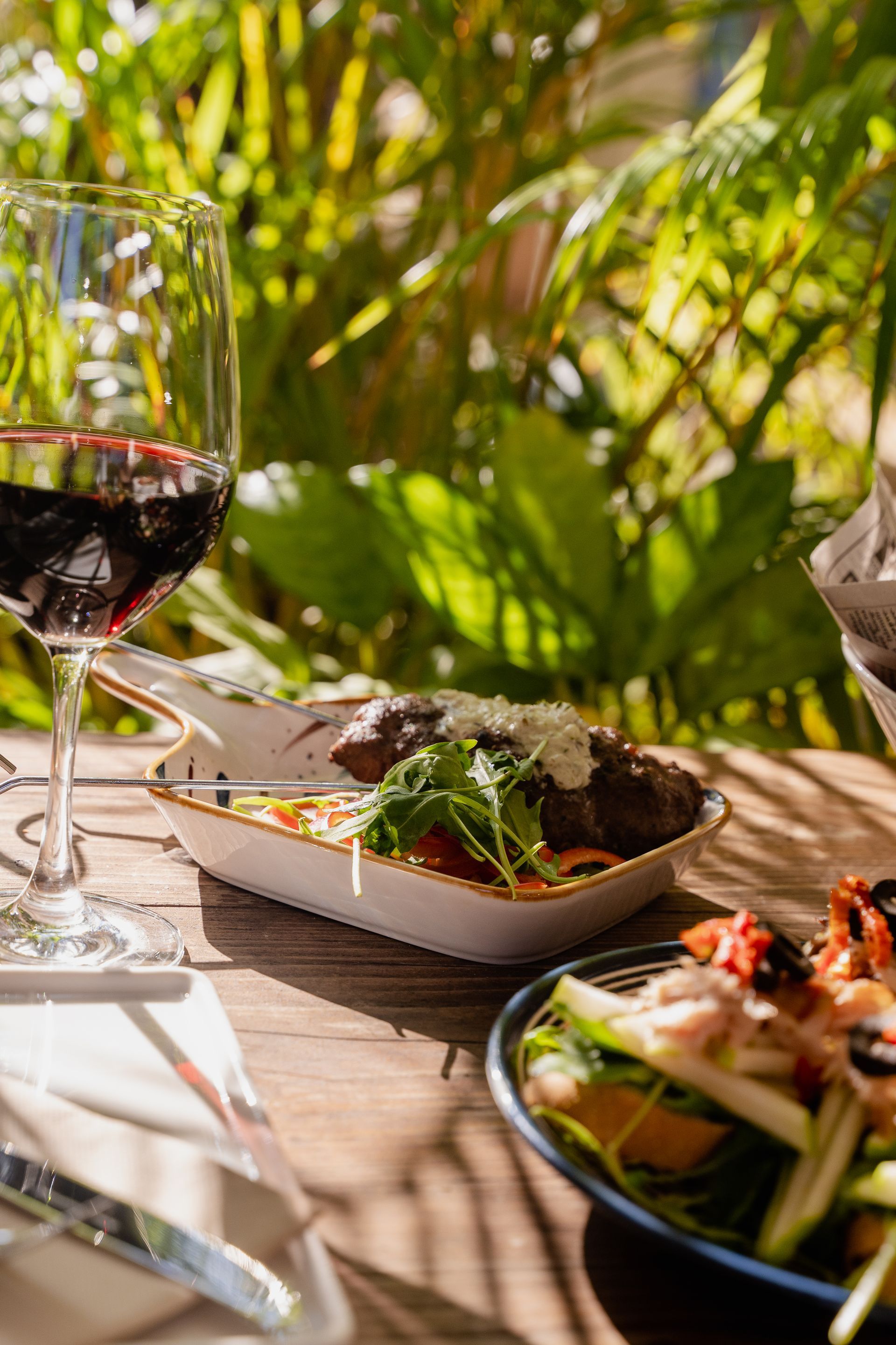 A wooden table topped with plates of food and a glass of wine.