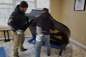 Two workers lift a black baby grand onto a dolley
