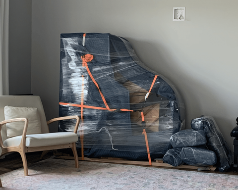 A wrapped baby grand sits on end against a wall in a home