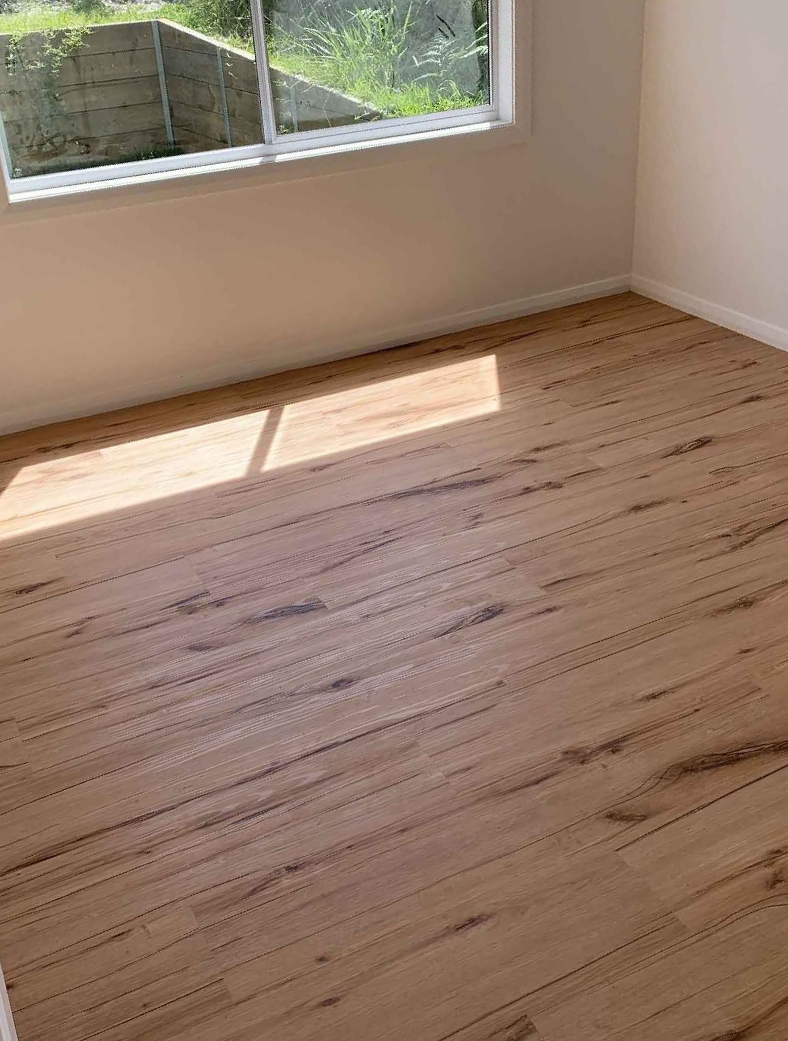 An Empty Room With a Wooden Floor and a Window — Bayside Carpets & Flooring in Laurieton, NSW