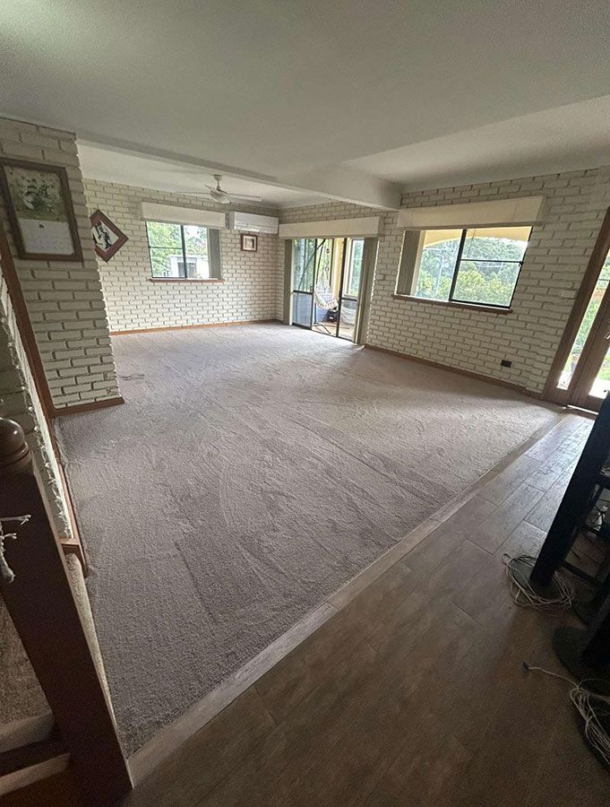 An Empty Living Room With a Carpeted Floor and Brick Walls — Bayside Carpets & Flooring in Wauchope, NSW