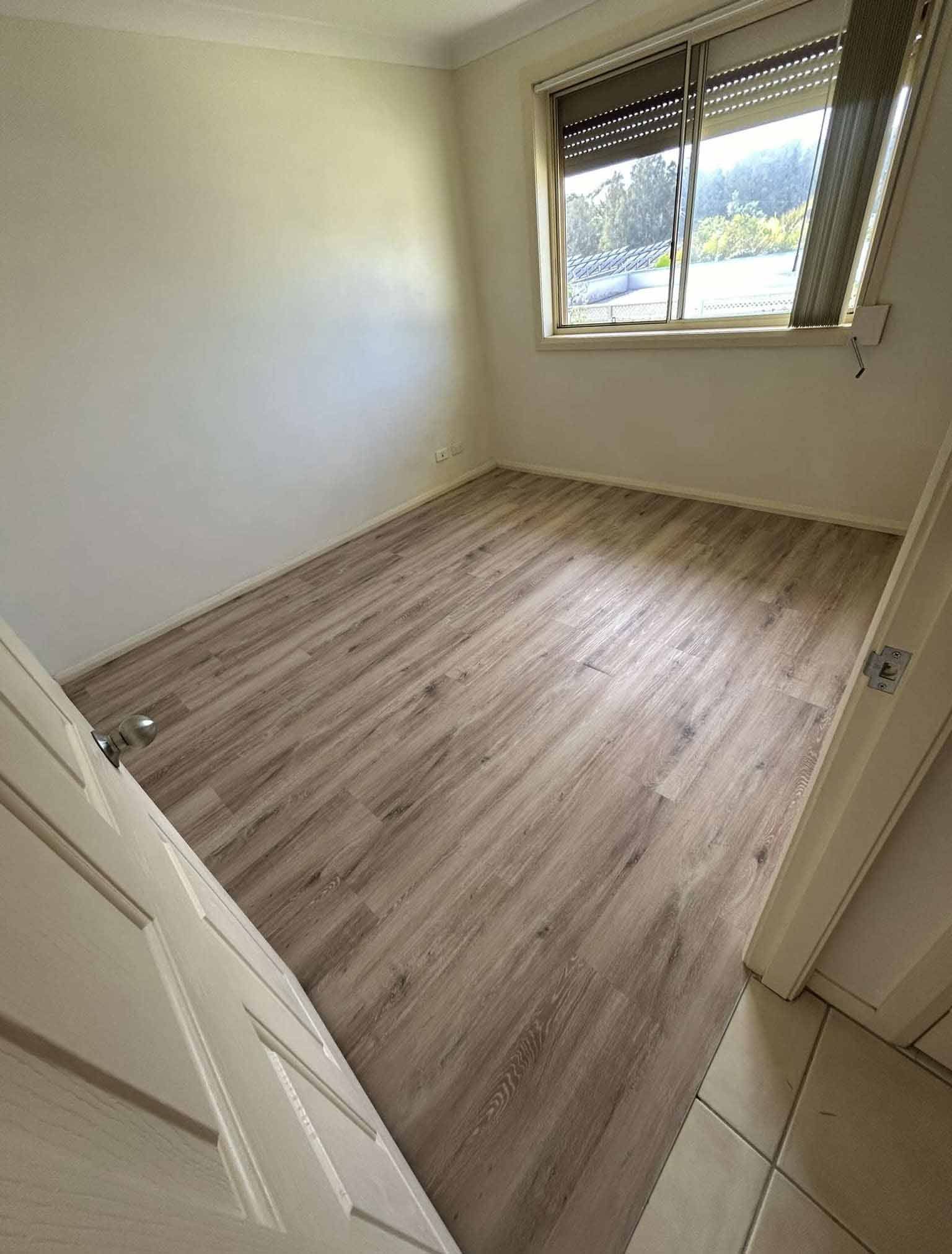 A Bedroom With a Wooden Floor and a Window — Bayside Carpets & Flooring in Laurieton, NSW