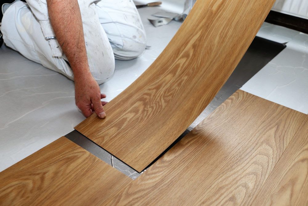 A Man is Laying a Piece of Vinyl Flooring on the Floor — Bayside Carpets & Flooring in Lake Cathie, NSW