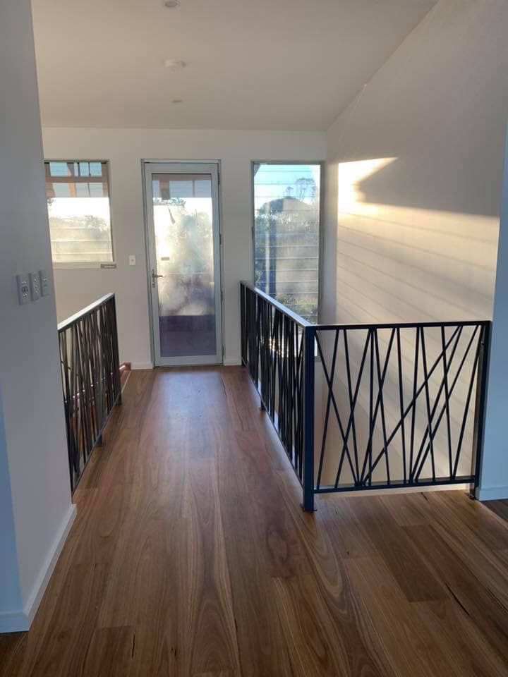 A Hallway With Hardwood Floors and a Metal Railing in a House — Bayside Carpets & Flooring in Laurieton, NSW