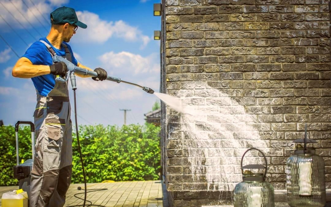 Worker spraying water from a hose at a stone wall beside a garden