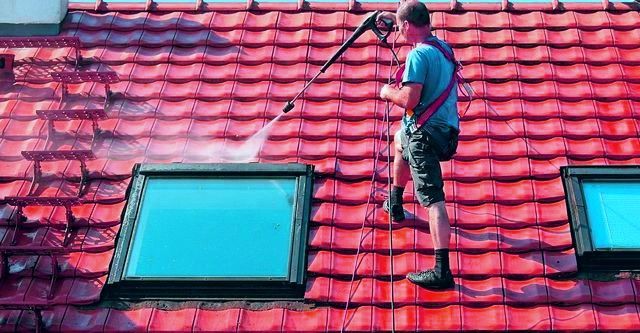 Worker pressure-washing a red tiled roof near skylights