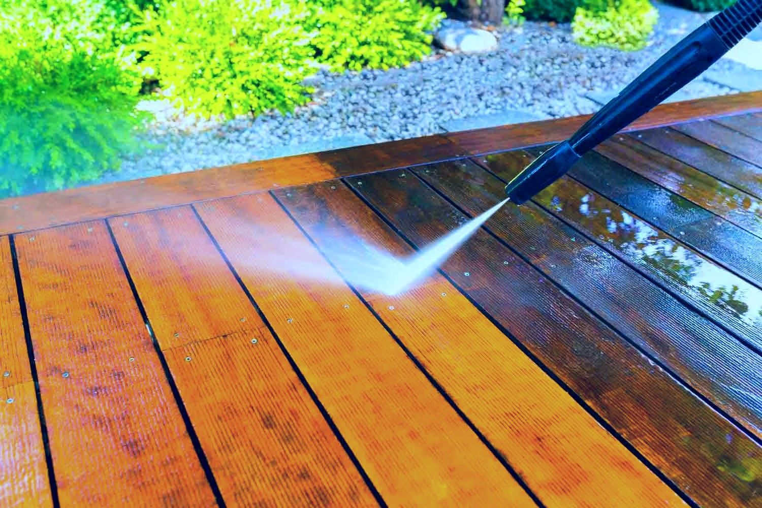Pressure washing a wet wooden deck beside a green garden