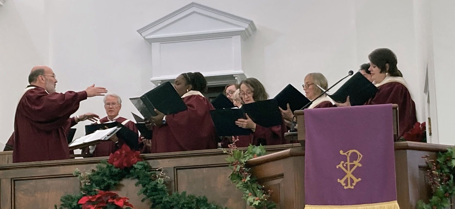 A choir is singing in a church with a man standing behind them.