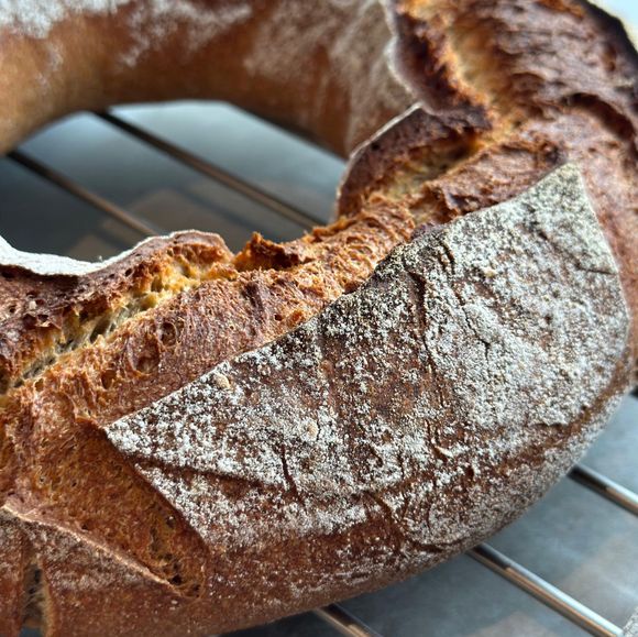 Primo piano di una pagnotta rustica a ciambella con crosta infarinata su una griglia di raffreddamento.