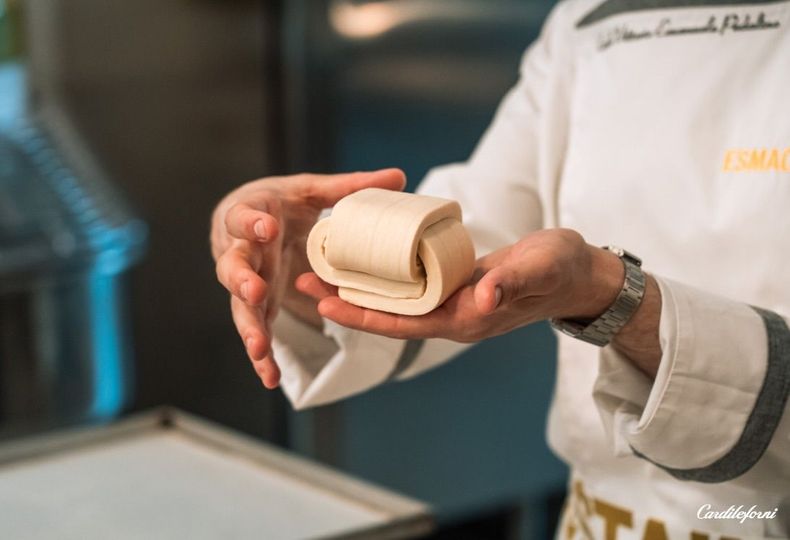 Uno chef tiene in mano un rotolo di pasta sfoglia sopra un vassoio in cucina.