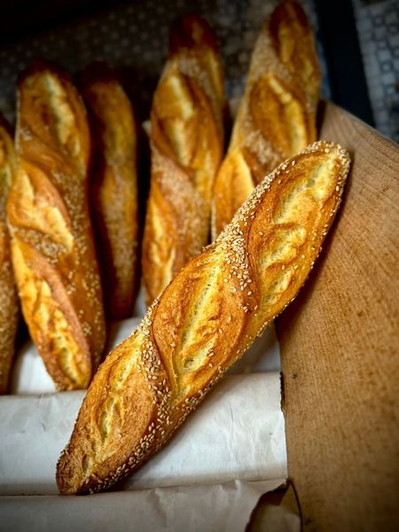 Mano che tiene una pagnotta rotonda di pane rustico dalla crosta croccante, con della farina bianca screpolata in superficie.