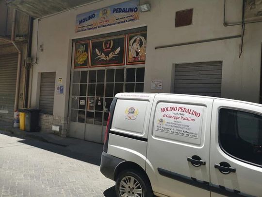 Una mano regge un panino intrecciato al sesamo sopra una griglia di raffreddamento con diversi tipi di pane fresco.