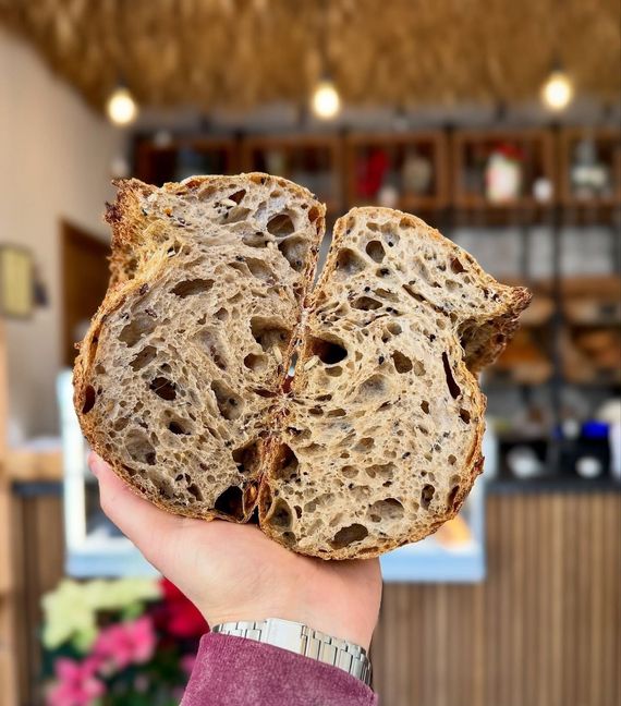 Una mano che regge una pagnotta rustica affettata in un accogliente interno di panetteria.
