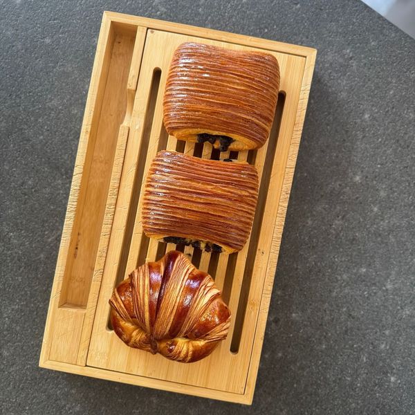 Tre pasticcini assortiti in un vassoio di legno su un piano di lavoro scuro.