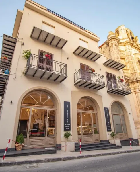 Edificio bianco a tre piani con finestre ad arco e balconi, situato su una strada stretta accanto al campanile di una chiesa.