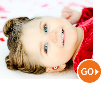Smiling child with blue eyes lying on a white blanket, orange “GO” button in the corner Smiling child with blue eyes lying on a white blanket, orange “GO” button in the corner