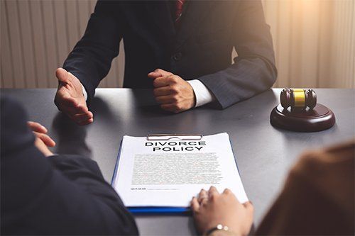 Lawyer with clients reviewing a divorce policy document at a table, gavel present.