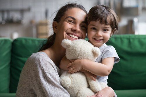 Woman and child smiling, embracing a teddy bear on a green couch.