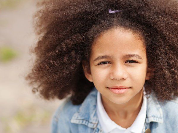 Girl with large, curly hair smiles, wearing a denim jacket and white shirt.