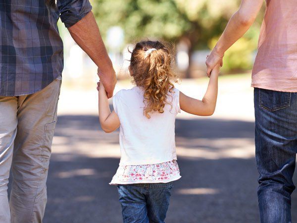 Child holding hands with two adults walking on a paved road.