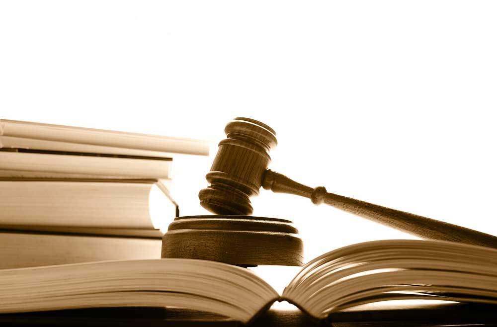 Wooden gavel on a sound block with open book in front; stack of books in background.