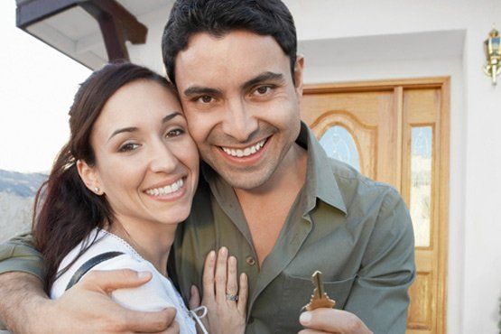 Smiling couple hugging, holding house key in front of a house.