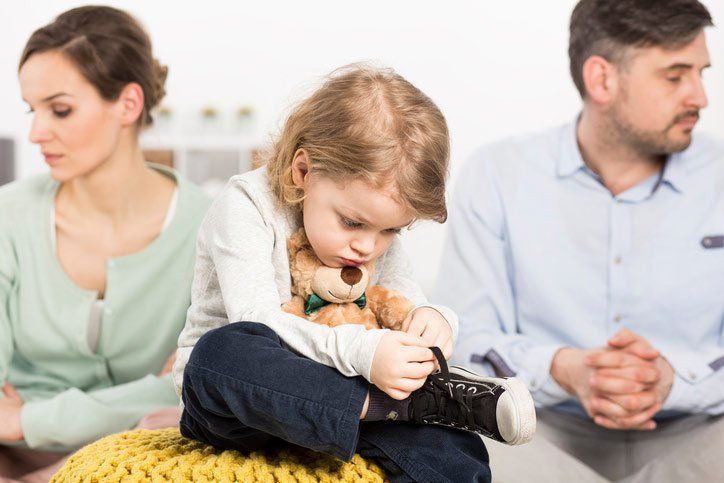 Child sits between parents, looking down while parents look away.