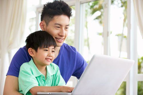 Man and child smiling while looking at a laptop computer. Indoors, natural light.