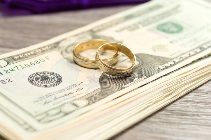 Two gold wedding rings rest on a stack of US twenty-dollar bills.