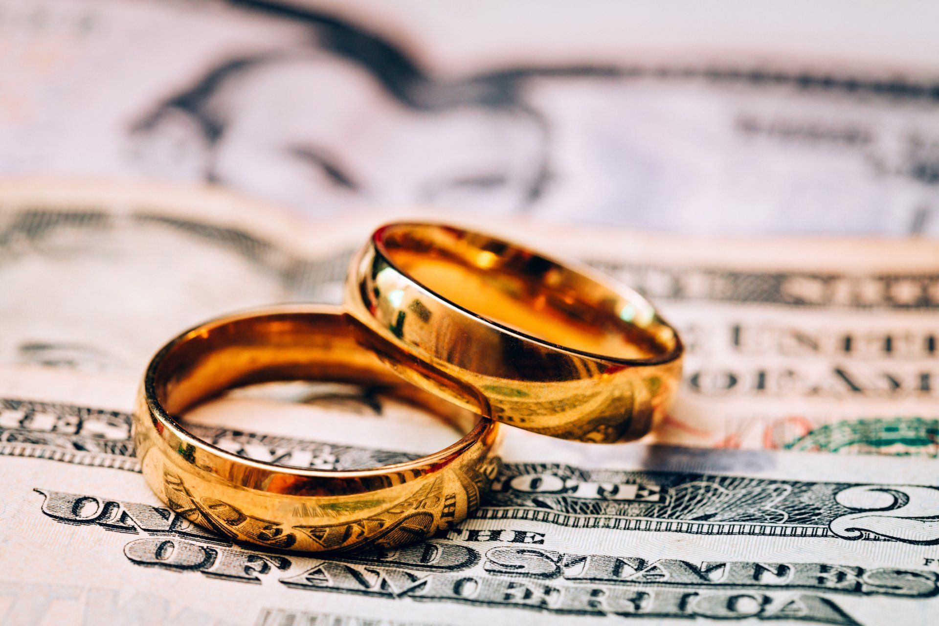 Two gold wedding rings rest on top of US dollar bills.