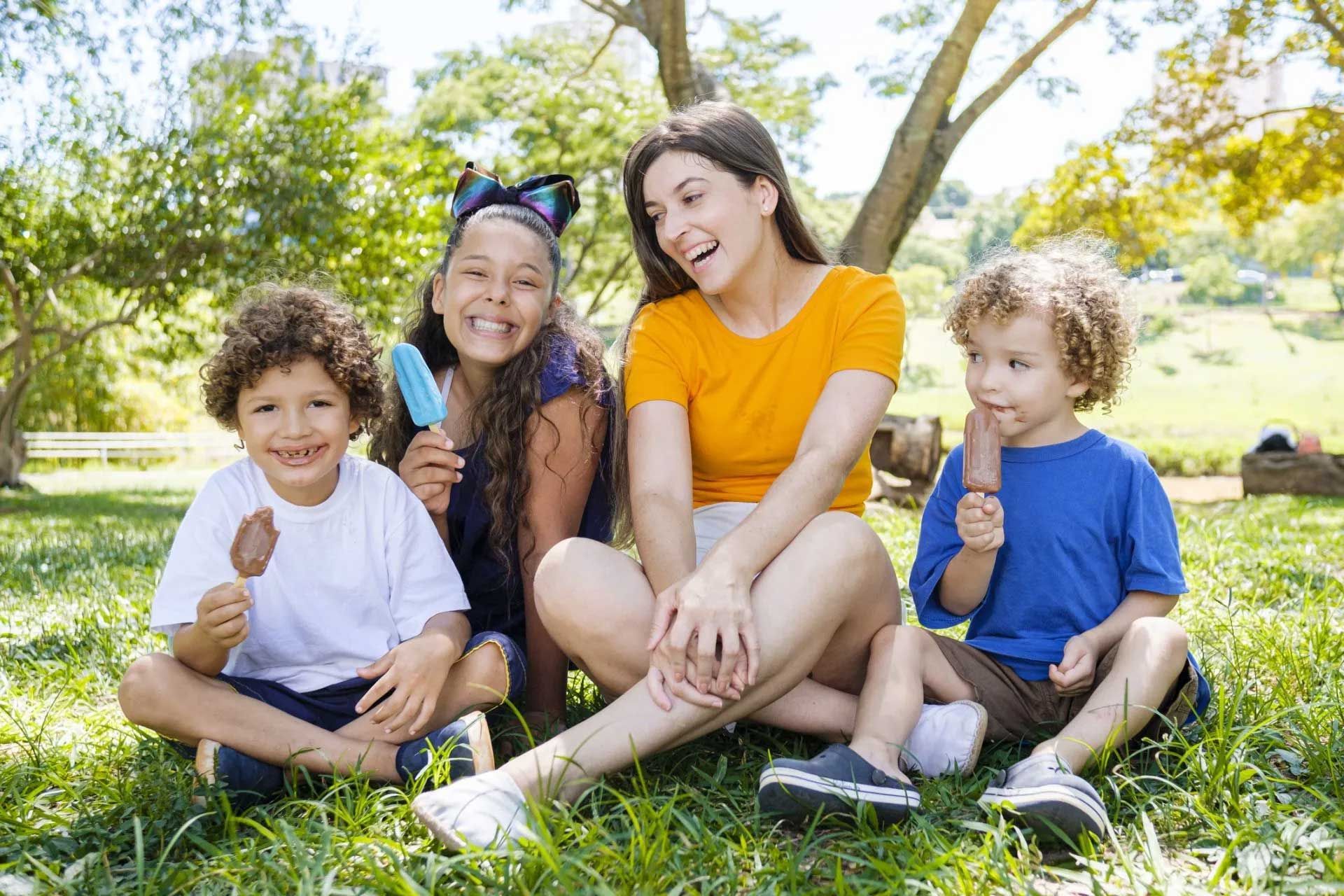 Happy Family — Wilmington, NC — Tise Allan Brandon Four people in a park eating ice cream. Two children and an adult smile at the camera.