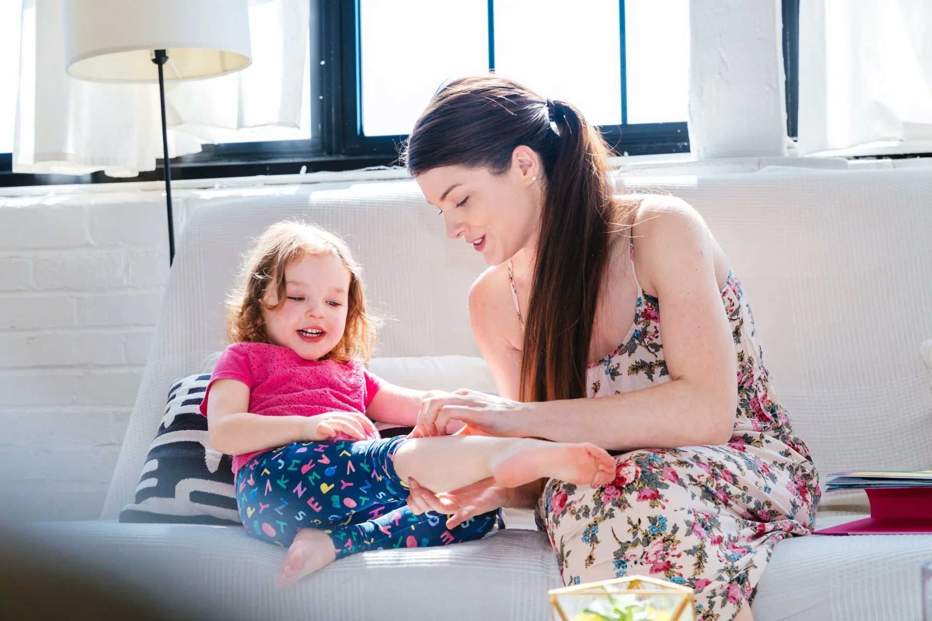 Woman on couch interacts with a toddler. The toddler smiles. Bright room.