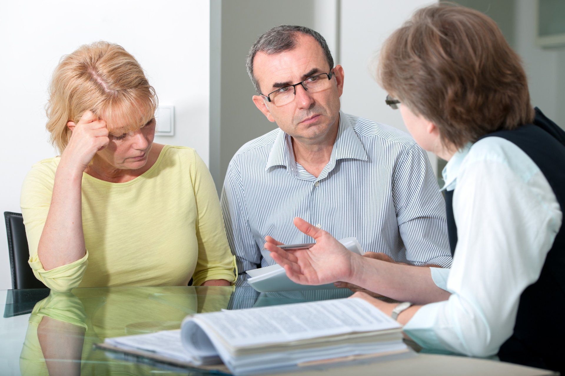 Couple at table listening to a person; woman in yellow looks distressed.