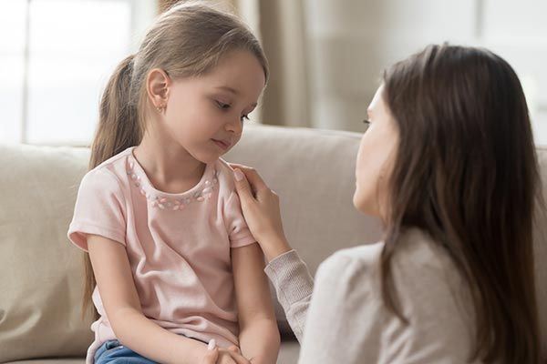 Woman comforting a young child, touching her shoulder.