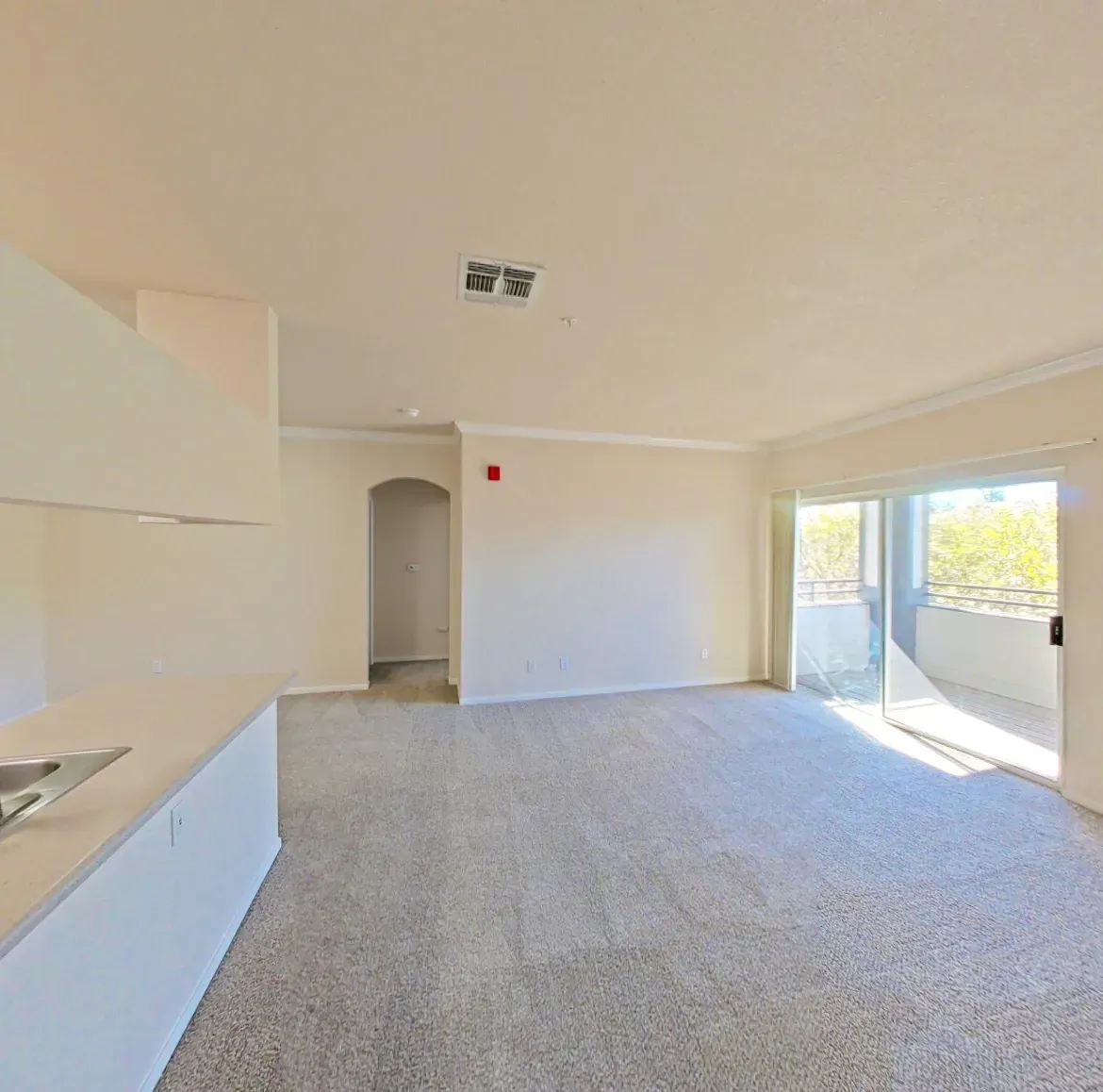 Living room and kitchen area of an apartment with sliding glass doors leading to a balcony.