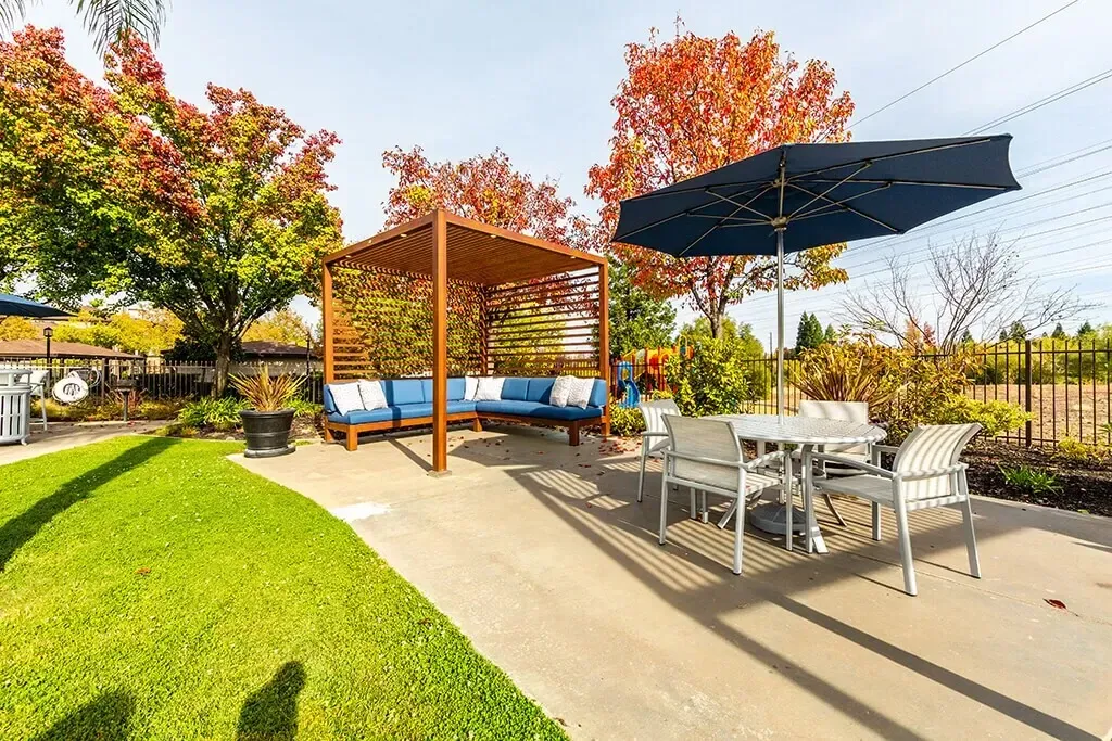 Outdoor seating area with a pergola, couch, and dining table with umbrella.