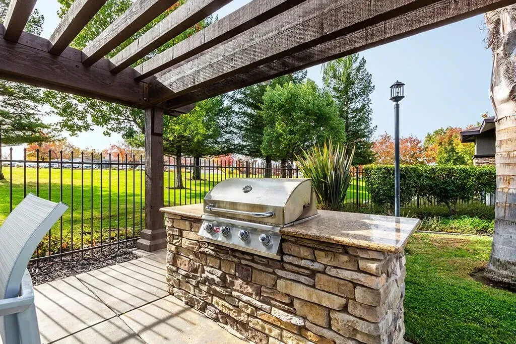 Outdoor BBQ grill station with stone counter and pergola.