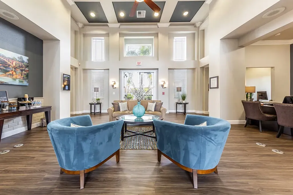 Lobby area with two blue chairs facing a sofa, coffee table, and entrance.