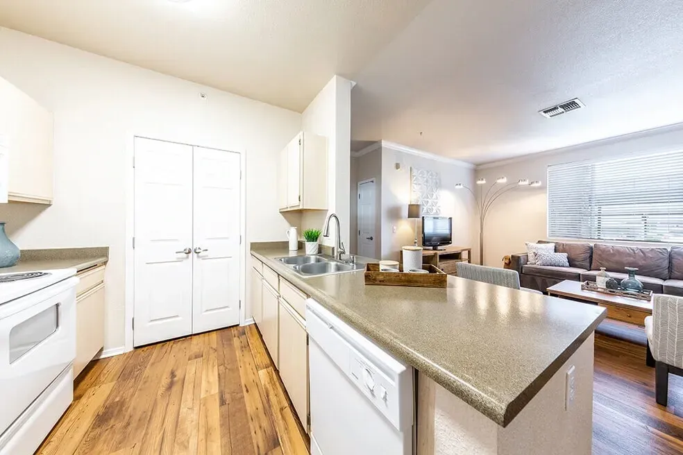 Modern kitchen with white appliances, double sink, and a view into the living room.