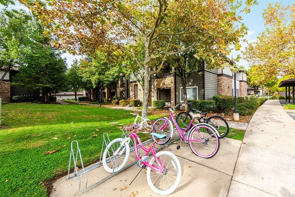 Bicycles parked outside apartment buildings with green grass and trees.