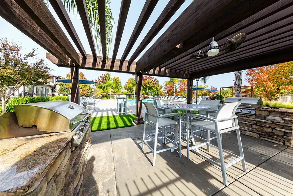 Outdoor grilling station with built-in grills, bar seating, and a dining table near the pool.