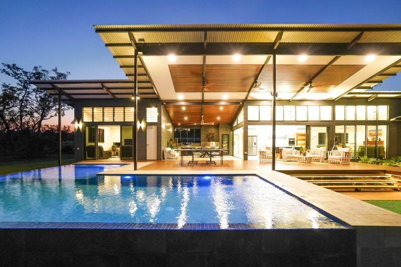 Modern house with a lit swimming pool at dusk and a covered patio with warm interior lights — Invision NT in Gove, NT