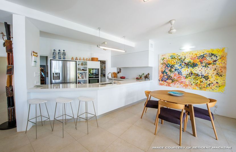 Bright modern kitchen and dining area with white cabinets, bar stools, and colorful abstract wall art — Invision NT in Gove, NT