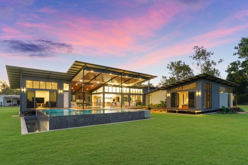 A modern, single-story home with a swimming pool and large glass windows under a vibrant pink and orange sunset sky. — Invision NT in Coconut Grove, NT