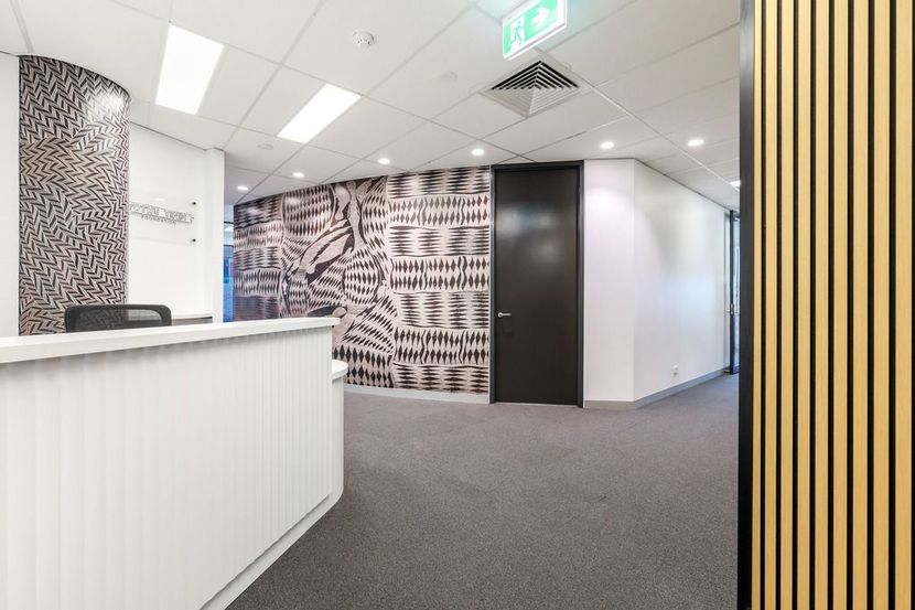 Modern office reception area with white desk, gray carpet, black-and-white mural, and striped wall paneling — Invision NT in Gove, NT