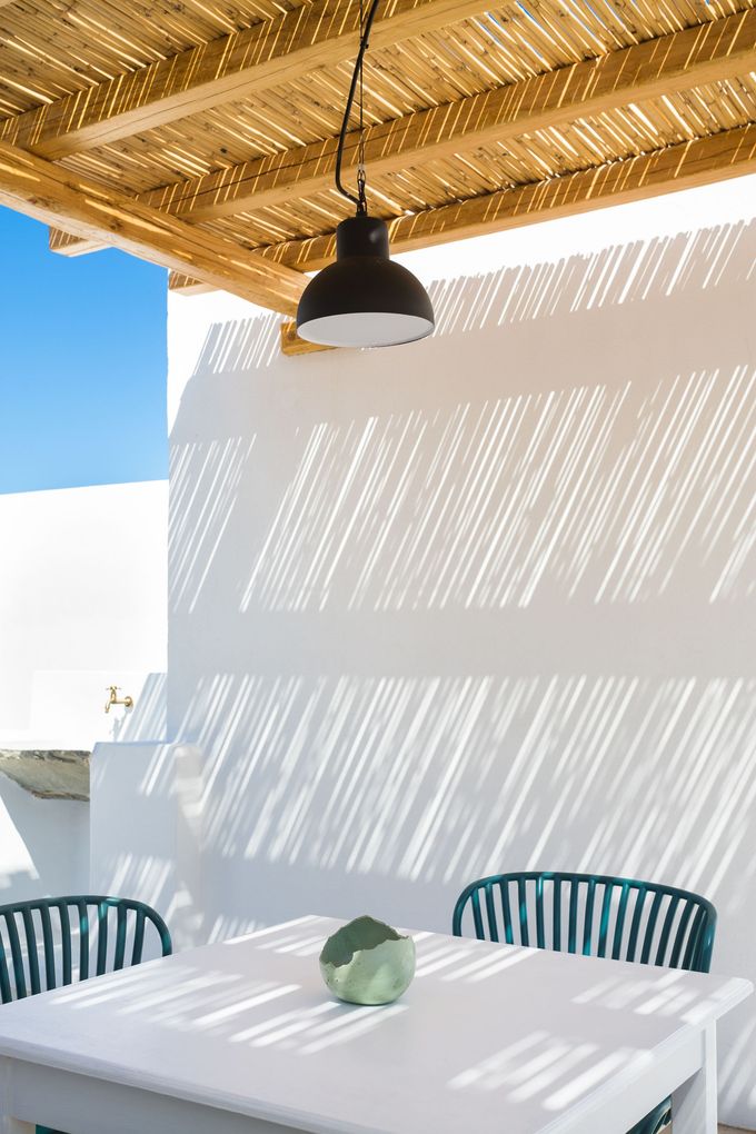 A white table and chairs under a wooden roof with a lamp hanging from the ceiling.