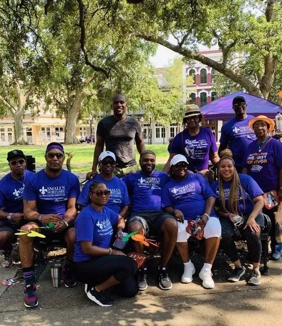 A group of people wearing blue shirts posing for a photo in a park under large trees.