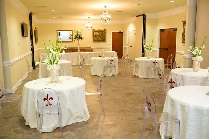 Event room set with round tables, white linens, chairs with fleur-de-lis accents, and floral centerpieces.