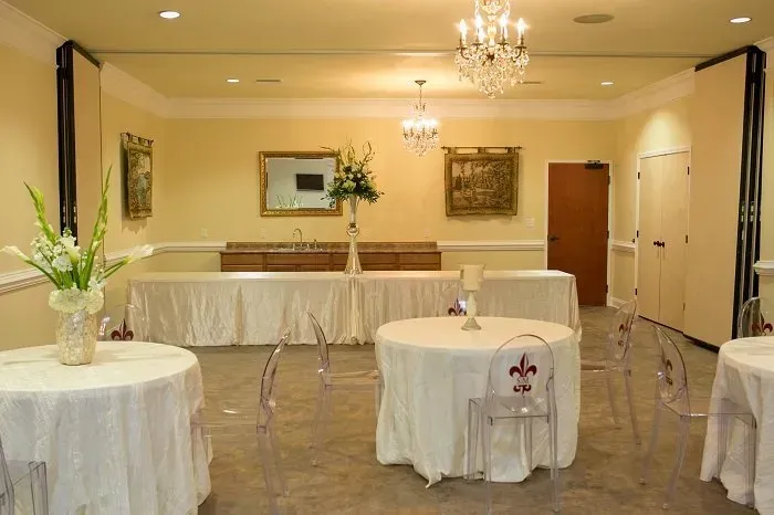 A ballroom featuring white-clothed round tables, a long head table with floral decor, chandeliers, and cream-colored walls.