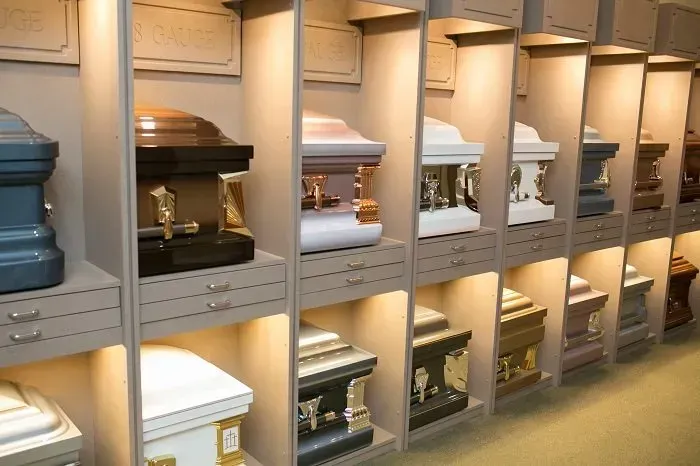 A showroom display featuring rows of various colored metal caskets arranged on shelves with internal lighting.